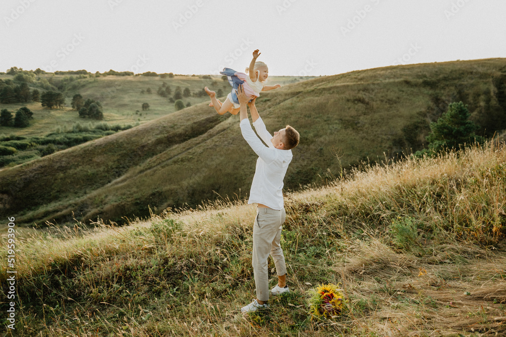 A young dad with a little daughter hugging, kissing and walking across the field at sunset. A young dad with a little daughter hugging, kissing and walking across the field at sunset.