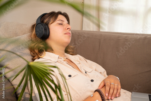 Jolie jeune femme allongée dans son canapé. Elle se repose en écoutant de la musique ou en regardant un film avec son ordinateur et un casque photo