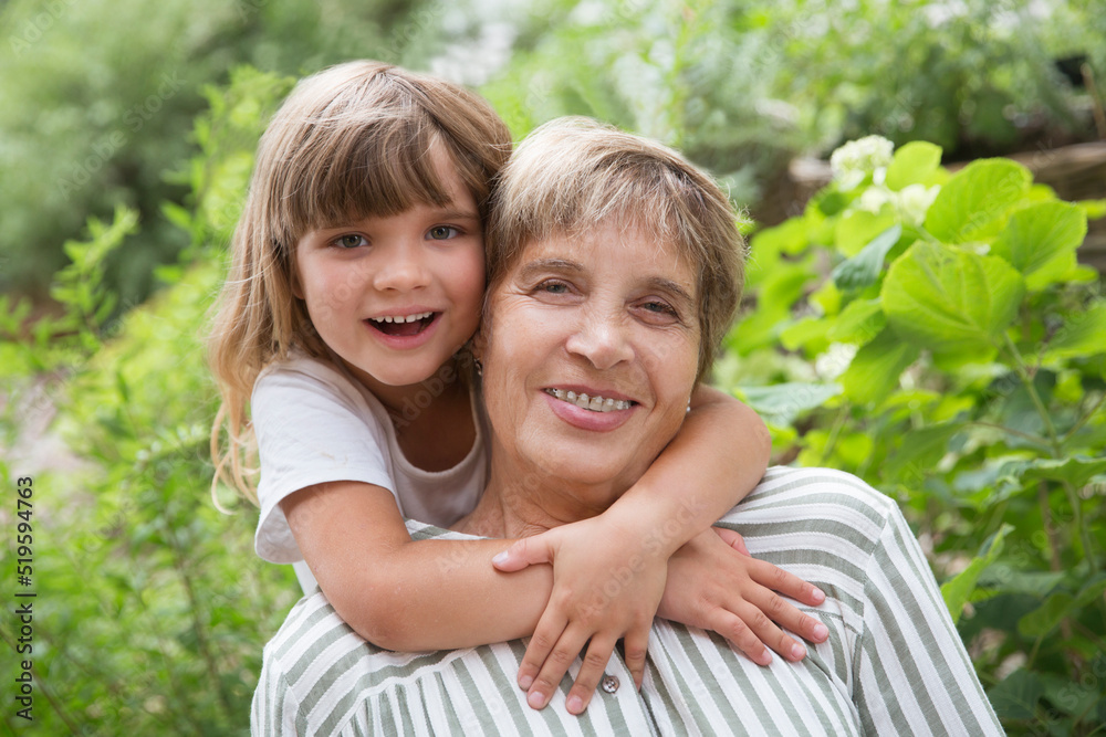 grandmother and little granddaughte hag and having fun together in the garden. Happy family enjoying summer outdoors. grandmother and little granddaughte hag and having fun together in the garden. Happy family enjoying summer outdoors.