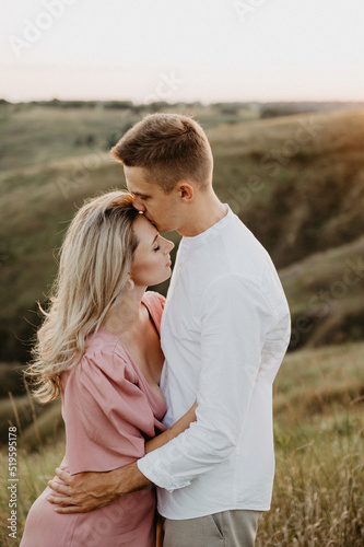 Beautiful woman and man are hugging and kissing on the field at sunset. A young couple hugging and kissing on a field at sunset.