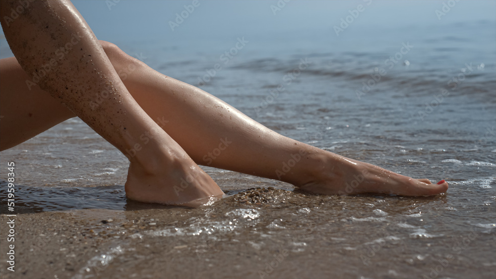 Sexy girl feet washed by sea waves close up. Barefoot woman sinking legs in sand Sexy girl feet washed by sea waves close up. Barefoot woman sinking legs in sand