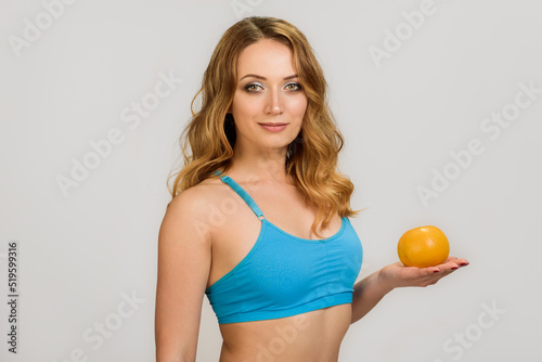 Portrait of attractive sportive young girl holding orange on palm