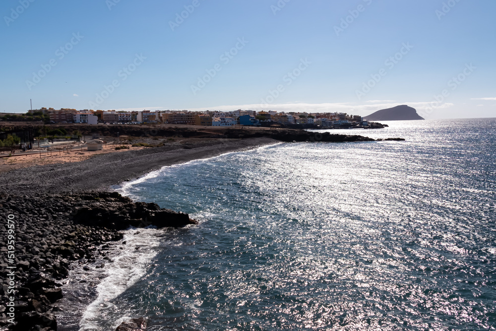 Obraz premium Panoramic early morning view on beach Playa de San Blas near coastal village Los Abrigos, Tenerife, Canary Islands, Spain, Europe, EU. Coastline of the Atlantic Ocean. Red mountain in the distance