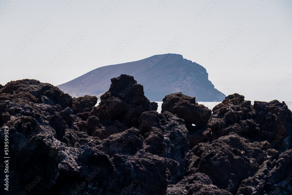 Panoramic early morning view on the Red Mountain (La Montana Roja) near Los Abrigos, Tenerife, Canary Islands, Spain, Europe, EU. Rocky coastline of the Atlantic Ocean. Selected focus on lava stones