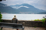 Female Tourist sitting on a bench looking out onto Lake Como Italy during a cloudy day