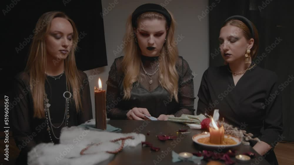 4K. Three female witches in a dark room reading tarot cards 4K. Three female witches in a dark room reading tarot cards