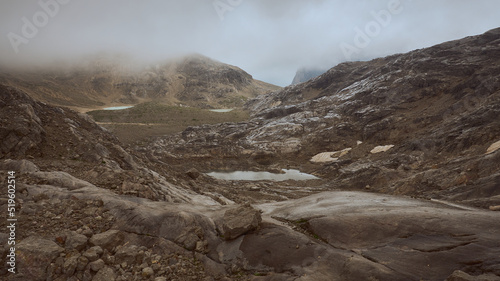 barren mountain landscape like on Mars with overcast sky, low hanging cloud, billowing fog an reddish brown limestone carved by massive glaciers