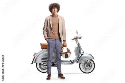 Full length portrait of a young man with curly hair holding a helmet and standing next to a scooter