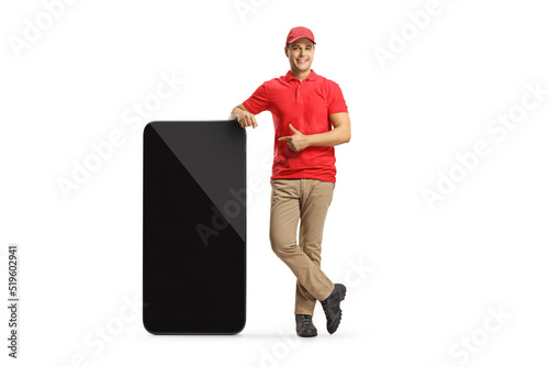 Full length portrait of a delivery guy standing next to a big mobile phone and pointing photo