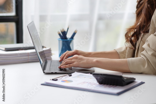 Business woman in office working with laptop and financial documents on desk.