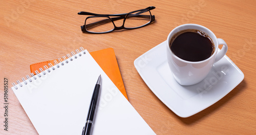 Side view of an office desk. Workspace with empty board, black framed glasses, pen and coffee cup on wooden background.