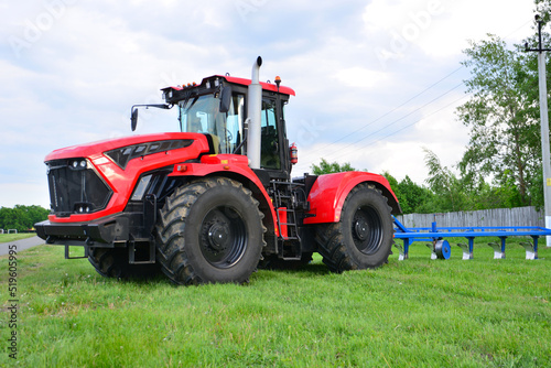 red tractor on green agricultural field with cloudy sky on background