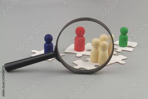 Magnifying glass with wooden people figures on white puzzles on gray background. Checking and control cooperation  team building and teamwork concept.