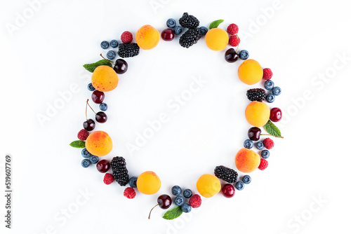 On a white background, fruits are laid out in a circle: apricots, cherries, blackberries, raspberries, blueberries, mint leaves.
