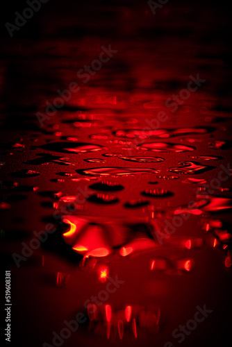 Beautiful macro photo of water drop reflection, lying on surface, front view. Close up of red liquid with side lighting from displays.