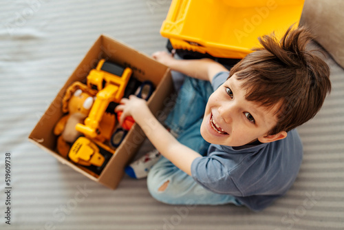 Tableau sur toile Portrait of happy caucasian boy packing toys in cardboard box donate to needy kids while sitting in living room at home during the day