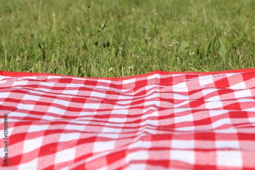 Checkered picnic tablecloth on fresh green grass, closeup