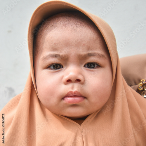 muslim little baby in brown hijab looking at the camera and frowning, dissatisfied with something