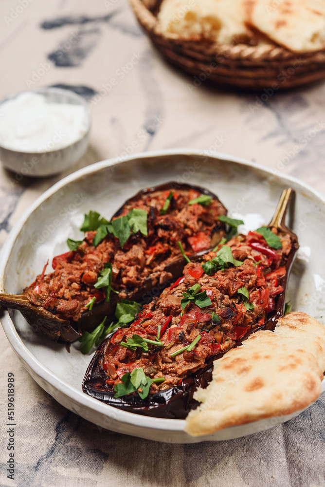 Imam bayildi. Traditional delicious Turkish food: halves of baked eggplant stuffed with vegetables on a plate. Selective focus Imam bayildi. Traditional delicious Turkish food: halves of baked eggplant stuffed with vegetables on a plate. Selective focus