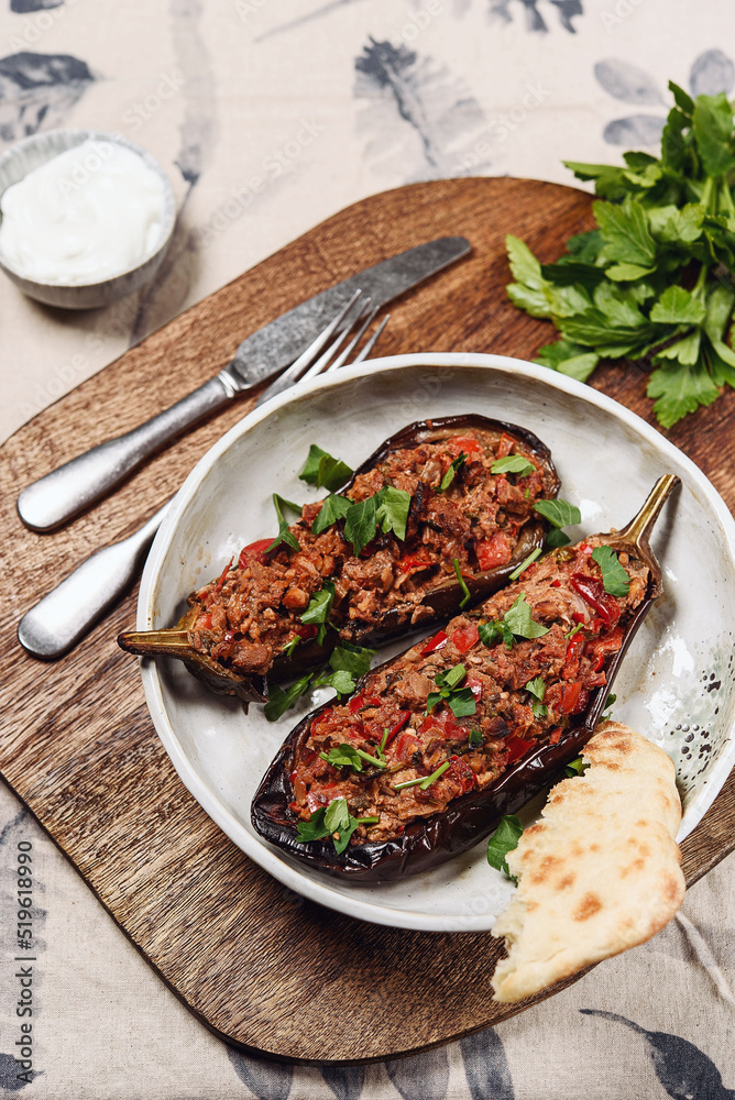 Imam bayildi. Traditional delicious Turkish food: halves of baked eggplant stuffed with vegetables on a plate. Selective focus Imam bayildi. Traditional delicious Turkish food: halves of baked eggplant stuffed with vegetables on a plate. Selective focus