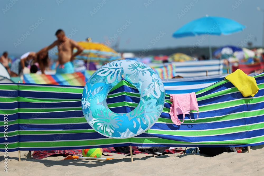 Parasol słoneczny na plaży nadmorskiej w wakacje razem z parawanem na wiatr.  - obrazy, fototapety, plakaty 