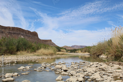 Cirrus clouds and cliffs in the background with the Rio Grande River and rocks at Big Bend Ranch State Park in Texas photo