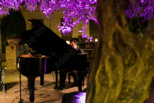 man playing the piano outdoors, purple illuminated tree in the foreground