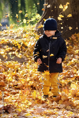 Happy child playing in yellow autumn leaves.