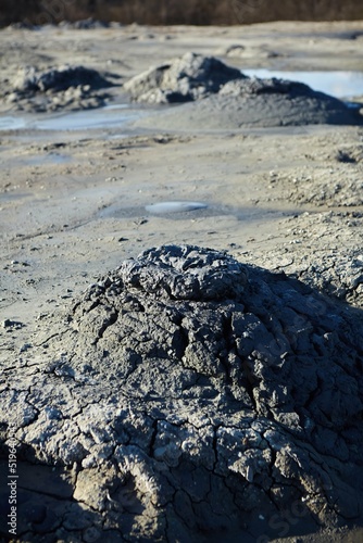 A mud volcano and a stream of grey clay from an eruption and gas escape. Cracked soil surface. Texture of a mudflow