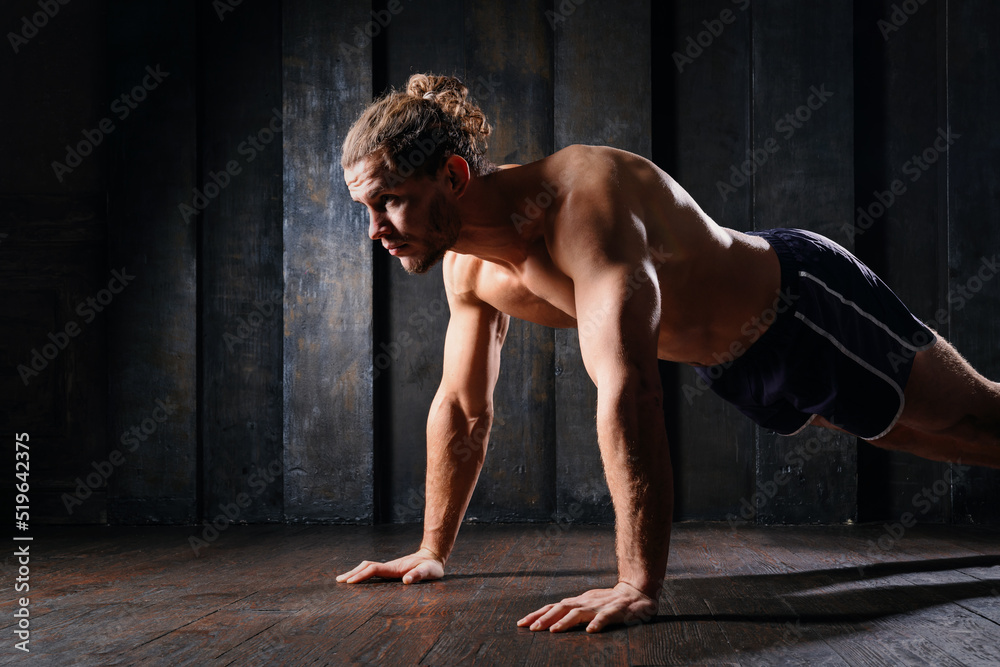 Obraz premium Young athletic guy in blue shorts on floor doing plank exercise on floor. Active strong fit sportsman do push-ups workout at gym with naked torso ripped shoulders. Sportive man, male, runner training