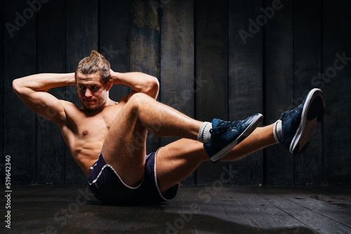 Fototapeta Naklejka Na Ścianę i Meble -  Shirtless athlete do exercises on the floor, intense training on black background. Young sportsman building abdominal, press muscle. .Strong fit male. man doing twist abs workout indoor training.