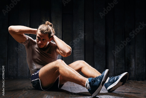 Active athlete do exercises on the floor, intense training on black background. Strong sportsman in sports clothing building abdominal, press muscle. Fit male do twist abs workout indoor training.