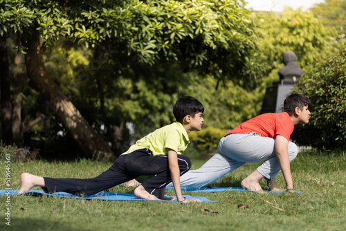 kids practices yoga & meditating outdoors in lawn or park or nature in springtime, beginner meditation, healthy lifestyle concept