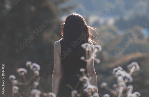 A young black-haired girl greets the sunset in the middle of the field. Romantic travel and nature beauty concept. Expectation of changes in life and dreams of meeting. View from the back