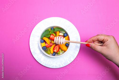  Fruit salad with wooden honey spoon on pink background