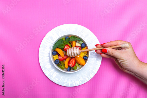 
Fruit salad with wooden honey spoon on pink background