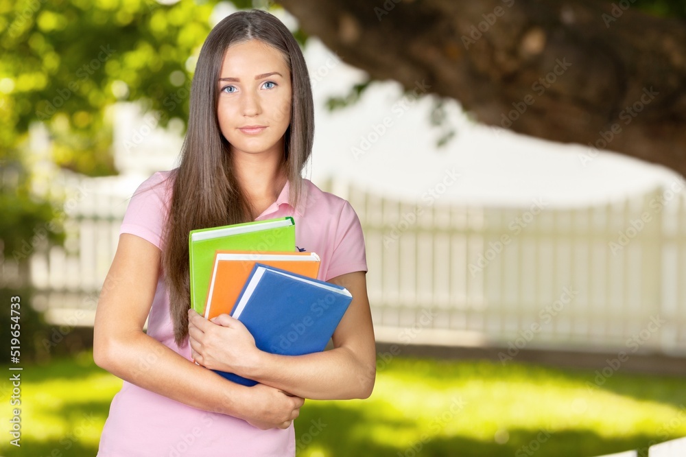 Portrait of a happy female student holding books and looking at natural outdoors Portrait of a happy female student holding books and looking at natural outdoors