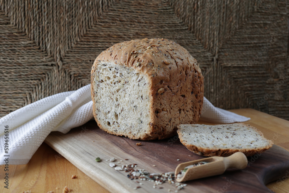 loaf of homemade whole grain bread and a cut slice of bread on a wooden ...