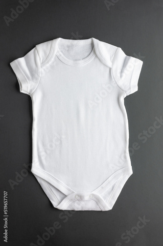 Flat lay of a white bodysuit made of natural fabric - basic clothing for newborn girls and boys on a gray background. Close-up. Flat layout for placement of logos, prints, advertising.