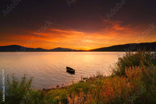 Fototapeta Naklejka Na Ścianę i Meble -  Samotna łódka unosi się na jeziorze podczas zachodu słońca