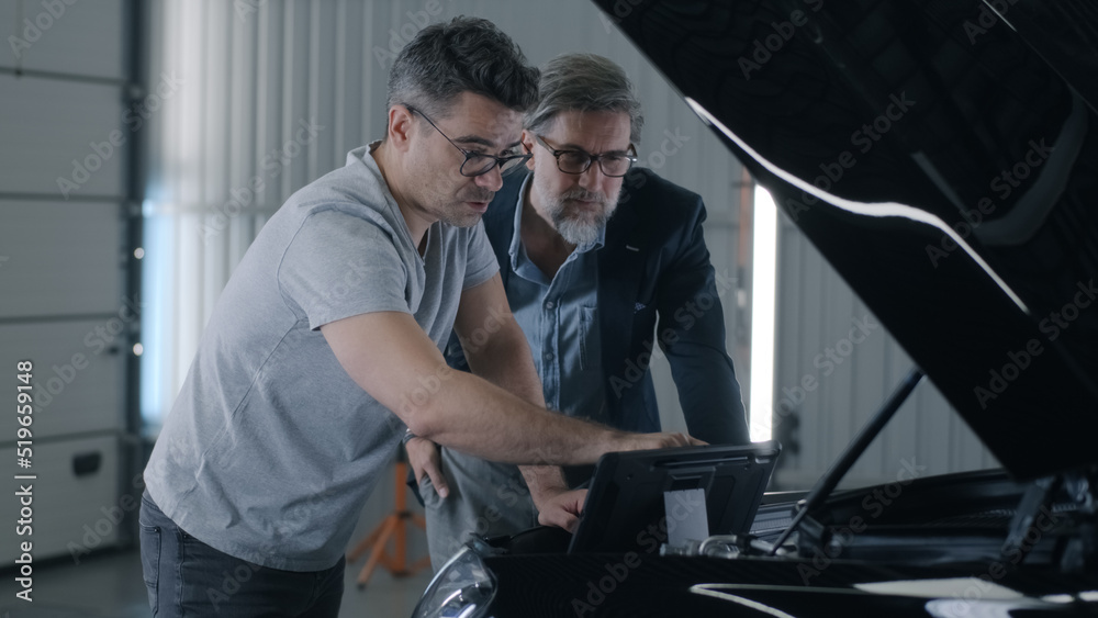 Man mechanic talking to client and checking car engine during diagnostics in car service using tablet computer Man mechanic talking to client and checking car engine during diagnostics in car service using tablet computer