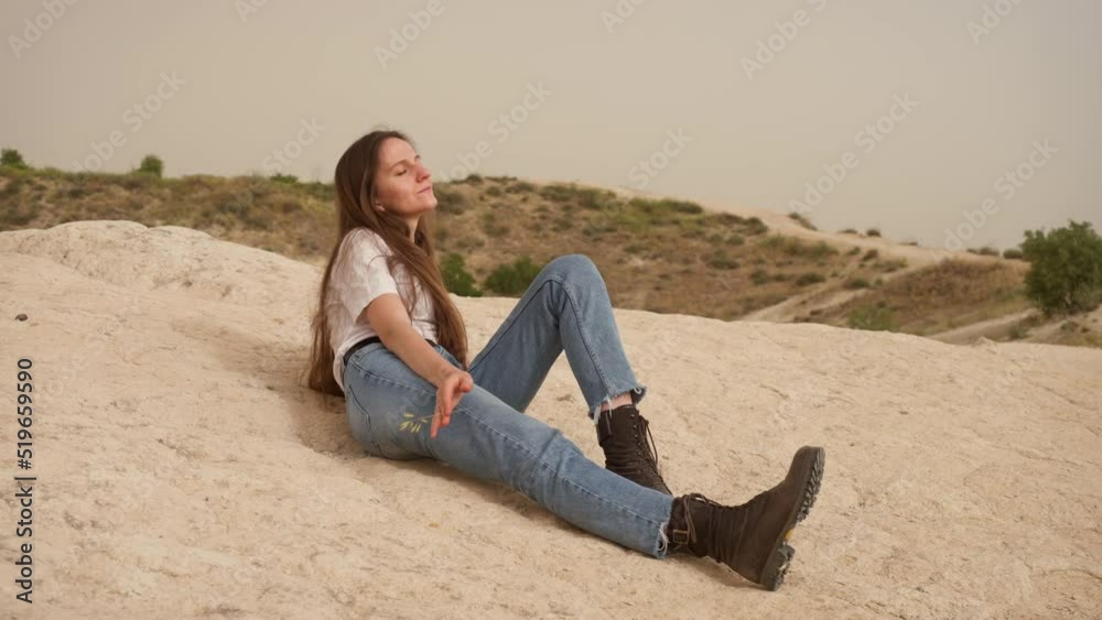 Relaxed woman with long hair and jeans lies on rocky hill slope in Cappadocia Relaxed woman with long hair and jeans lies on rocky hill slope in Cappadocia