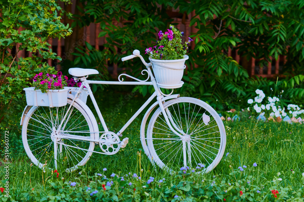 A white bicycle adorns a section of the park. Landscaping. Decorative flowers, grass and bushes. Selective focus.