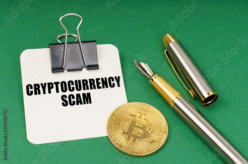 Fototapeta Naklejka Na Ścianę i Meble -  On a green surface, a bitcoin coin, a pen and a sheet of paper with the inscription - Cryptocurrency scam
