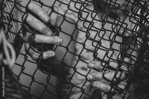 Hands of an old woman on a rusty fence, black and white photo, slavery and captivity, people