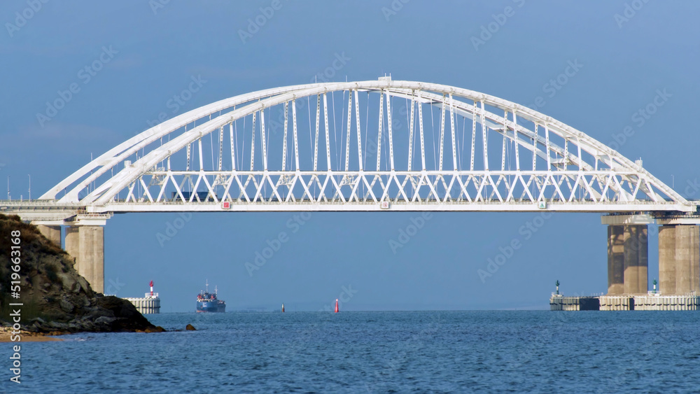 Obraz premium Breathtaking seascape with a white beautiful bridge with many moving cars above the water surface and sailing ships, time lapse effect. Shot. Calm sea with ripples, huge bridge, vessel and bue sky.