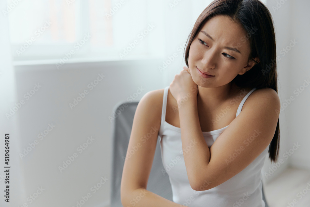 Suffering from shoulder dislocation neuralgia tanned beautiful young Asian woman touching painful shoulder at home interior living room. Injuries Poor health Illness concept. Cool offer Banner Suffering from shoulder dislocation neuralgia tanned beautiful young Asian woman touching painful shoulder at home interior living room. Injuries Poor health Illness concept. Cool offer Banner