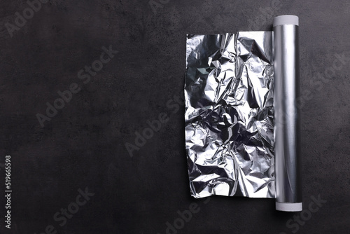 Roll of aluminum foil on dark grey table, top view. Space for text