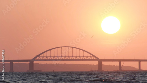 Amazing sunrise sky above the calm sea with ripples and white high bridge, beauty of nature. Shot. Golden sunrise above the horizon with time lapse effect.