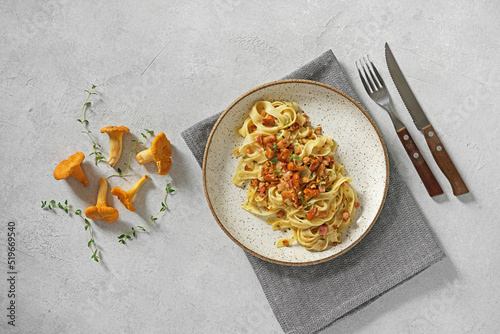Tagliatelle with chanterelles and bacon, on plate, on white stone background, top view